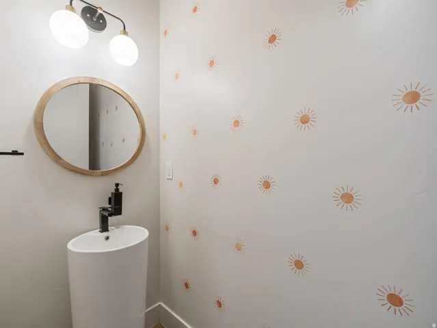 Pedestal sink with a matte black faucet, oval wooden-framed mirror, and a modern two-light vanity fixture