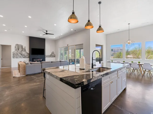 Spacious open-concept living area featuring a kitchen island with stone countertops, a built-in stainless steel sink, and pendant lighting
