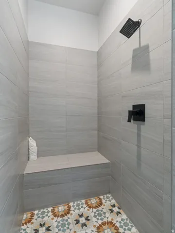 Tiled shower enclosure featuring a built-in bench, rain shower head, and matte black fixtures