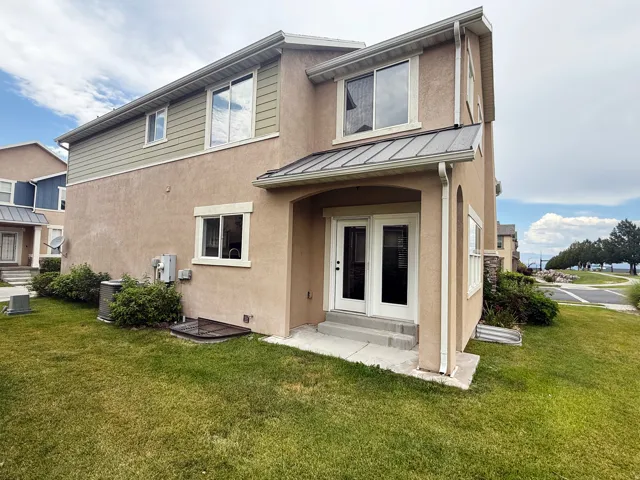 Rear exterior featuring a stucco finish, accent siding, and a metal awning over French doors
