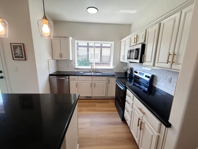 Kitchen featuring white cabinetry, black countertops, stainless steel appliances, wood-finish flooring, and subway tile backsplash