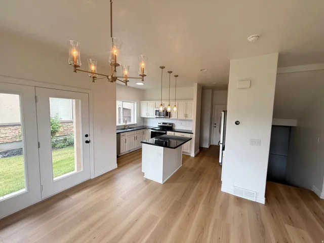 Open-concept kitchen and dining area featuring wood-finish flooring, white cabinetry, dark countertops, and stainless steel appliances