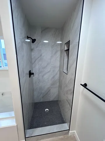Glass-enclosed shower featuring large-format marbled wall tile and black hexagonal mosaic floor tile