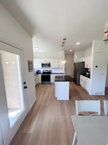 Kitchen featuring light wood-finish flooring, white cabinetry, dark countertops, a central island with pendant lighting, and stainless steel appliances