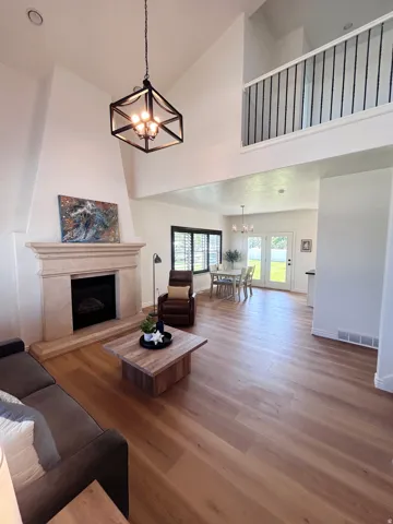 High vaulted ceilings with an open loft, stone-clad fireplace, wood-finish flooring, and French doors to the exterior