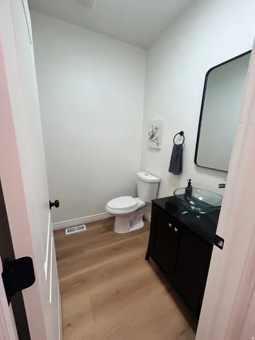 Powder room featuring wood-finish flooring, a contemporary black vanity with storage, a clear vessel sink, a sleek black-framed mirror, and a modern toilet
