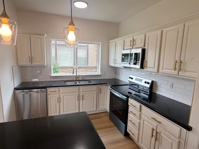 Kitchen featuring white cabinetry with gold-toned hardware, dark countertops, and a subway tile backsplash