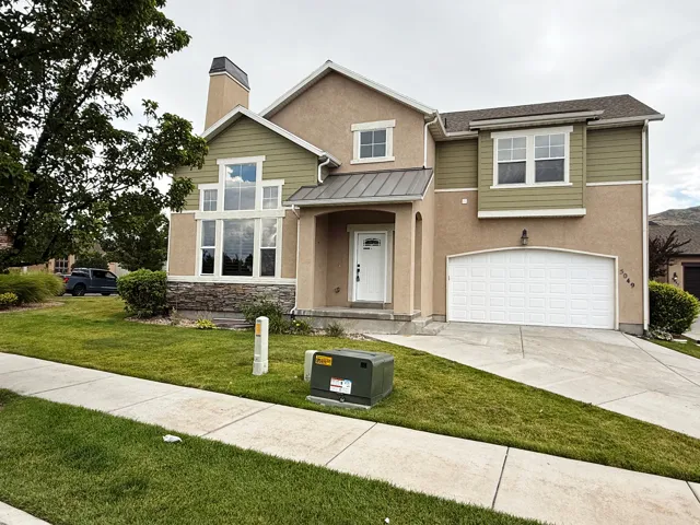 Stucco and siding exterior featuring a prominent two-story window arrangement, an attached two-car garage, stone accent detailing, and a covered entryway