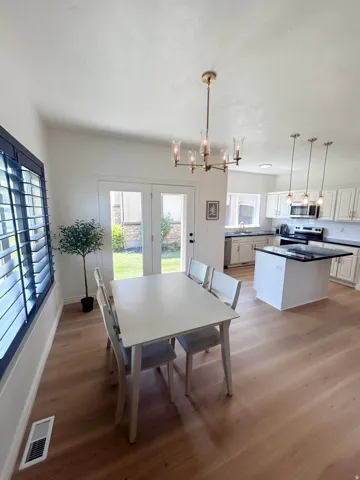 Open-concept living space with wood-finish flooring, white walls, and a modern chandelier