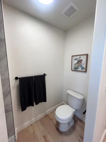 Recessed ceiling lighting, wood-finish flooring, white toilet, and tile shower surround