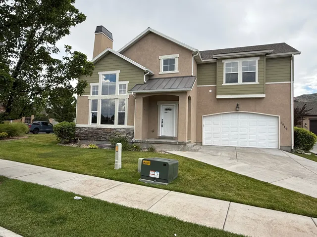 Two-story residence featuring a multi-tone stucco and siding exterior with stone accents, a prominent front entry, an attached two-car garage, large picture windows, and a landscaped front lawn