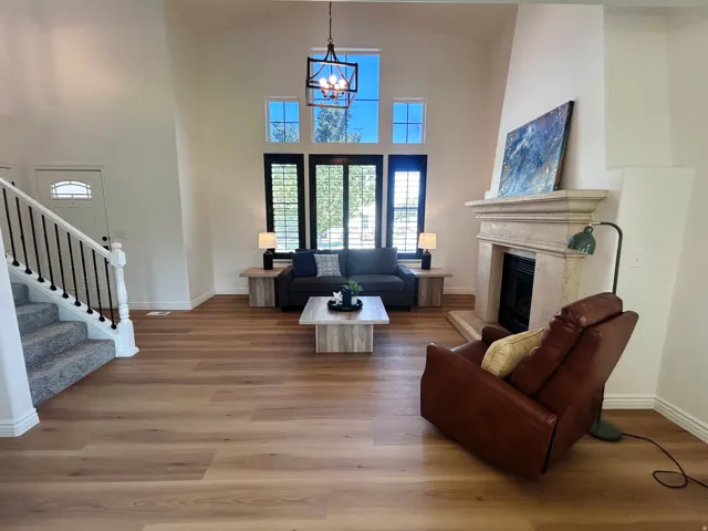 Vaulted ceilings with an open-concept design, wood-finish flooring, a stone fireplace, a staircase with wrought iron balusters, and transom windows