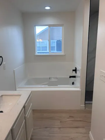Bathroom featuring a white built-in tub with matte black fixtures, a window above, and wood-finish flooring