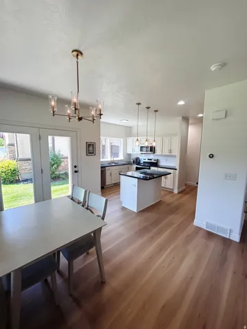 Open-concept living space with wood-finish flooring, a kitchen island, white cabinetry, and stainless steel appliances