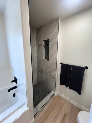 Walk-in shower with tile surround, black hexagonal floor tile, and built-in niche