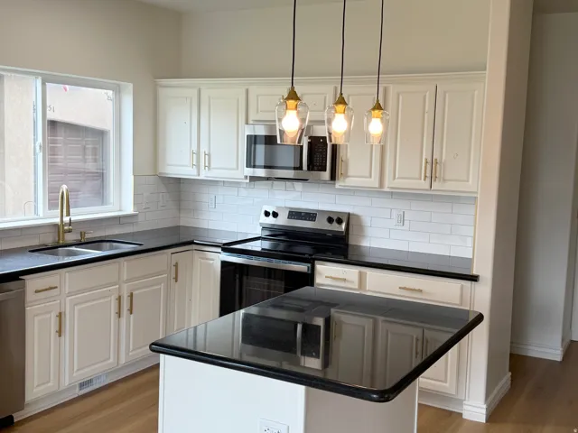 Modern kitchen featuring light cabinetry with gold-finish hardware, dark countertops, a subway tile backsplash, and stainless steel appliances