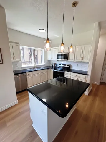 Kitchen featuring a center island with a dark countertop, light wood-finish flooring, white cabinetry, and stainless steel appliances