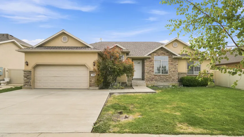 Ranch-style residence featuring a prominent stone and stucco facade, a two-car garage, a concrete driveway, and a front lawn