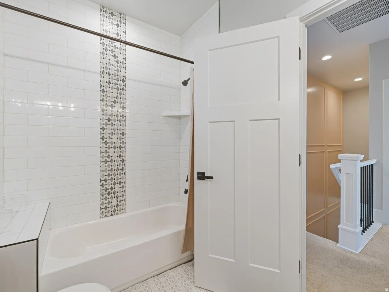 Bathtub and shower combination featuring a decorative mosaic tile inlay and white subway tile surround