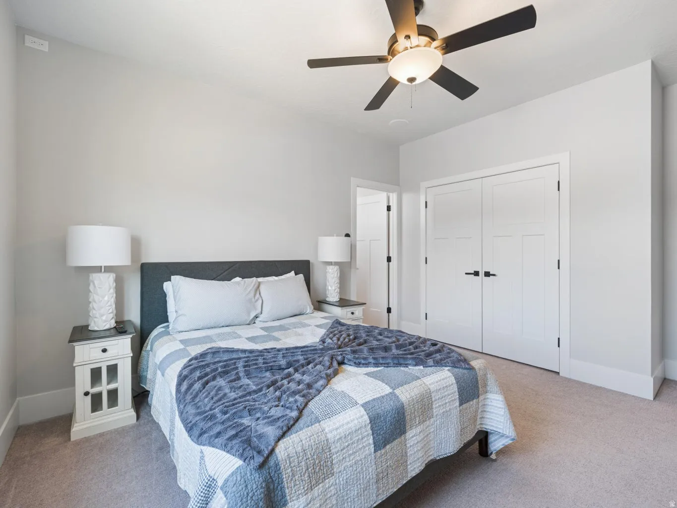 Carpeted room featuring a ceiling fan with integrated lighting, white baseboards, and two-panel interior doors with black hardware
