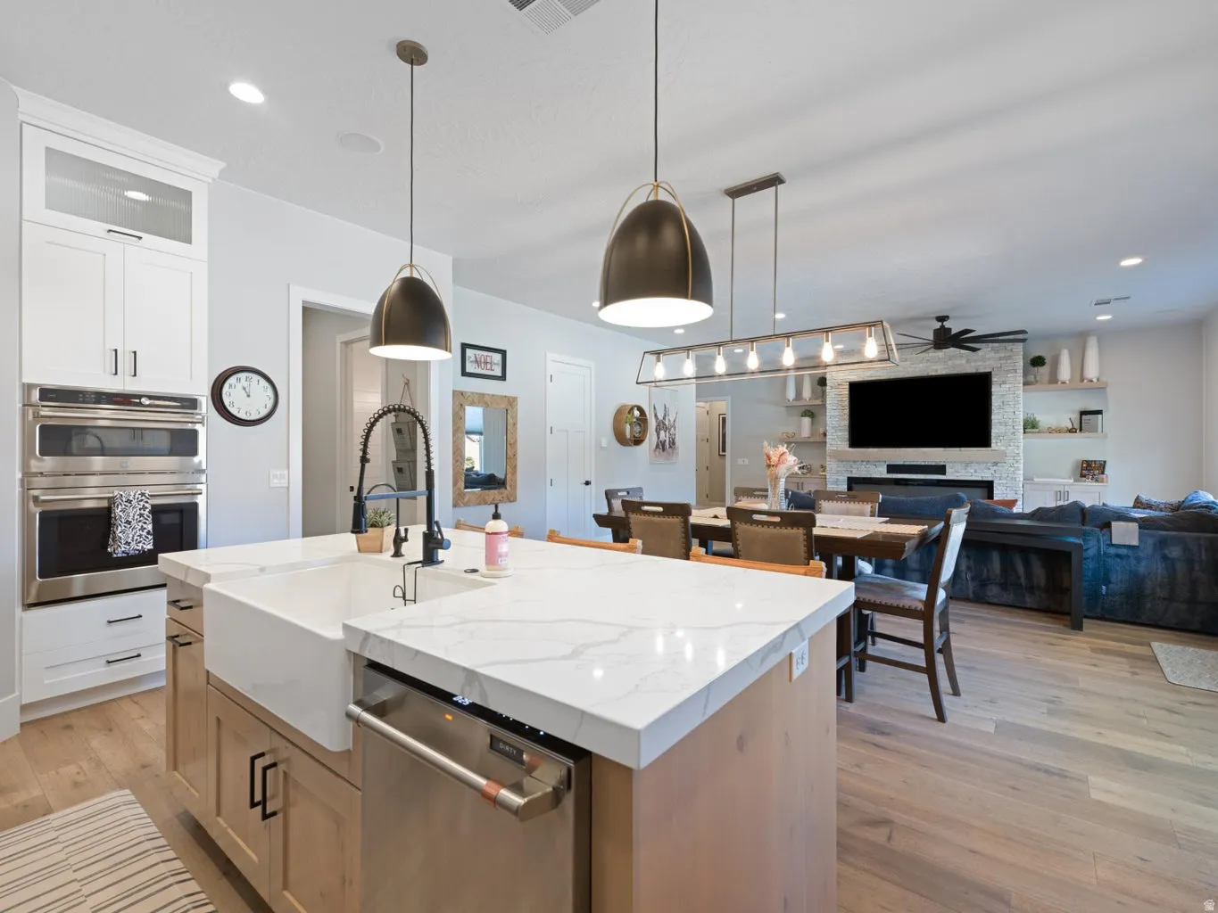 Gourmet kitchen island with a farmhouse sink and stone-finish countertop, double wall ovens, built-in cabinetry, and wood-finish flooring