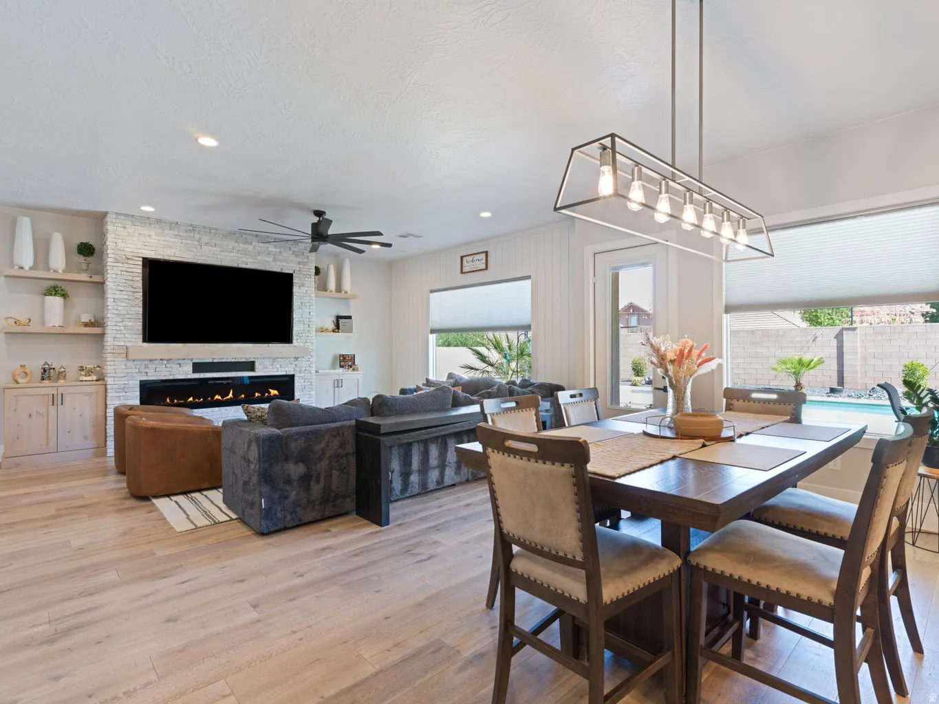Open-concept living area with wood-finish flooring, a stone-clad fireplace, and built-in shelving