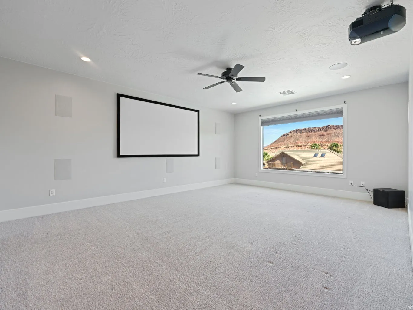 Dedicated media room featuring a large projection screen, mounted projector, recessed lighting, and integrated wall speakers