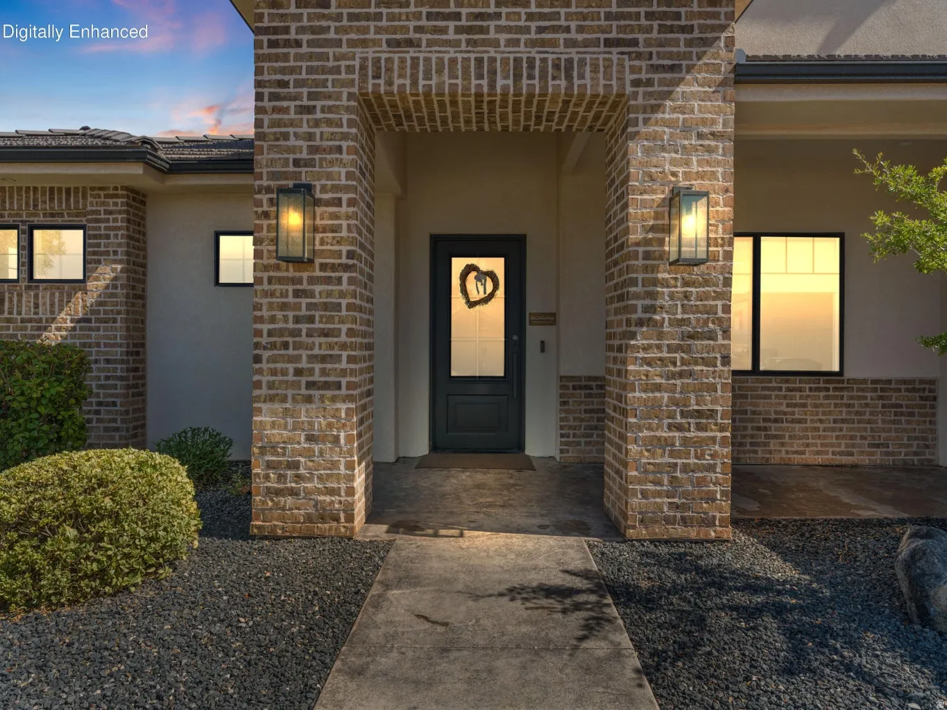 Brick facade entrance featuring a dark-paneled door with glass inserts, framed by built-in sconce lighting