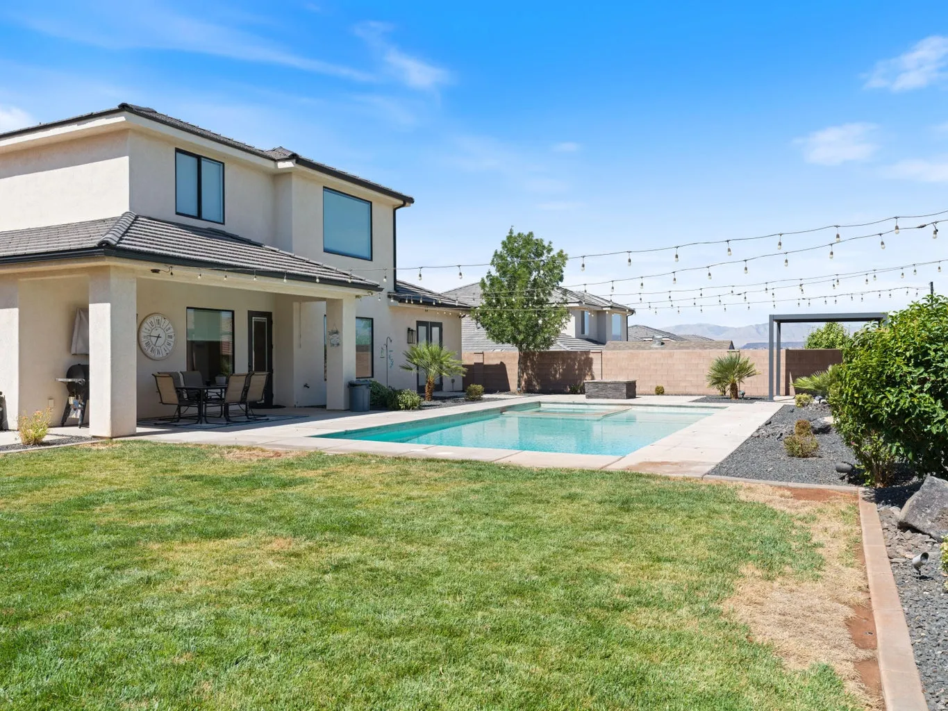 Expansive backyard featuring a rectangular swimming pool with surrounding concrete decking, a covered patio, and a grass lawn