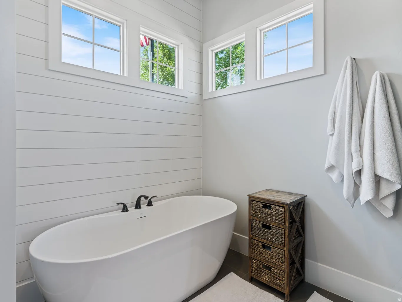 Freestanding soaking tub with matte black fixtures, shiplap accent wall, and natural light from upper windows