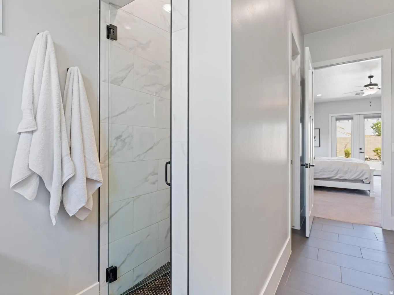 Contemporary glass-enclosed shower with large format tile surround and black penny tile flooring