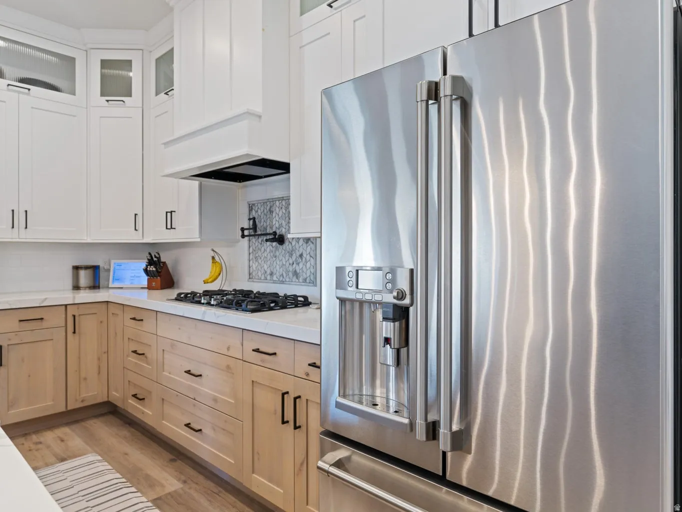 Gourmet kitchen featuring a stainless steel side-by-side refrigerator, gas cooktop, and a white range hood