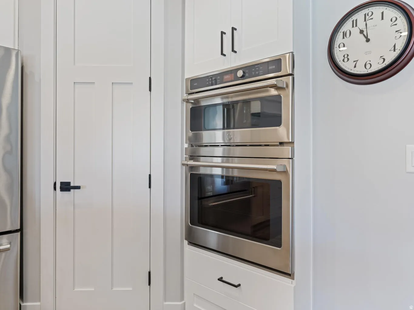 Built-in stainless steel double oven, integrated into white shaker-style cabinetry with matte black hardware