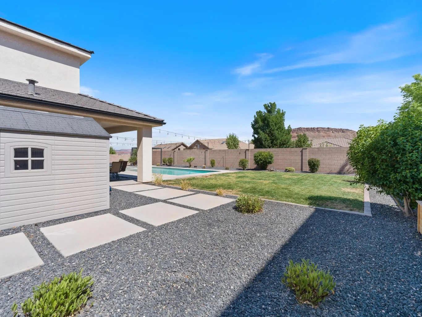 Expansive backyard featuring a rectangular swimming pool, covered patio, artificial turf, and dark gravel landscaping with concrete stepping stones