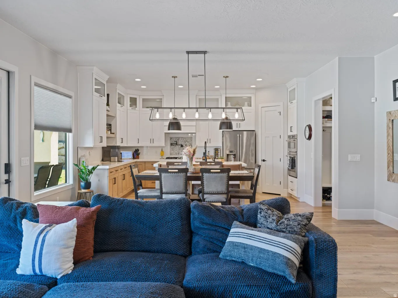 Open-concept kitchen and dining area featuring white cabinetry, light wood-finish flooring, a stainless steel refrigerator, and integrated double ovens