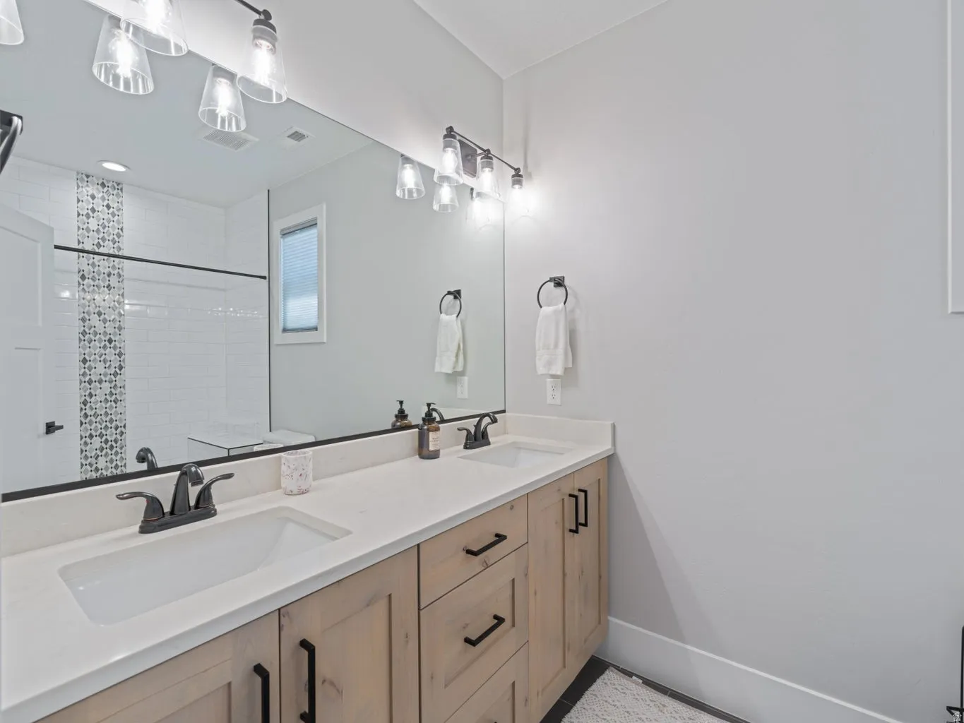 Dual vanity featuring light-toned wood-finish cabinetry, white countertops, and matte black fixtures