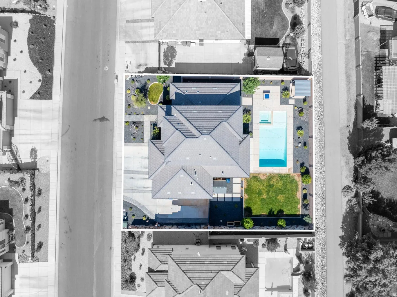 Aerial view showcasing a property with a distinct roofline, a private swimming pool, a spa, a square of manicured lawn, and paved patios