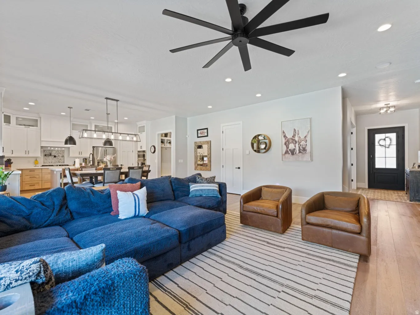 Open-concept living area with light wood-finish flooring and a black multi-blade ceiling fan