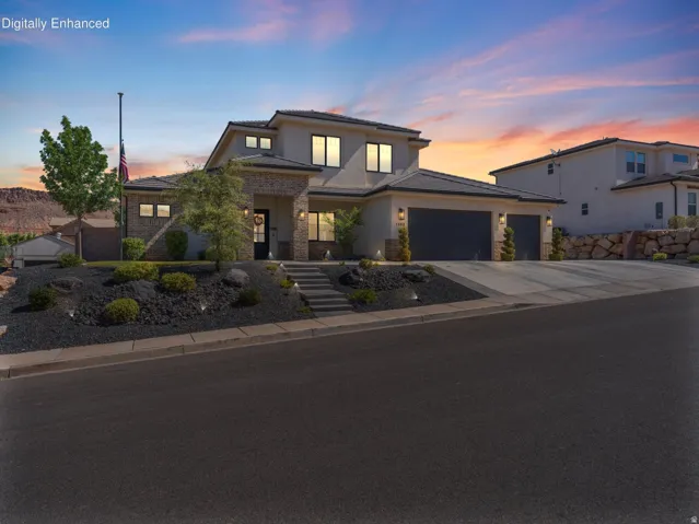Modern stucco exterior with stone accents, featuring a multi-car garage, established front landscaping, and a tiered stone retaining wall