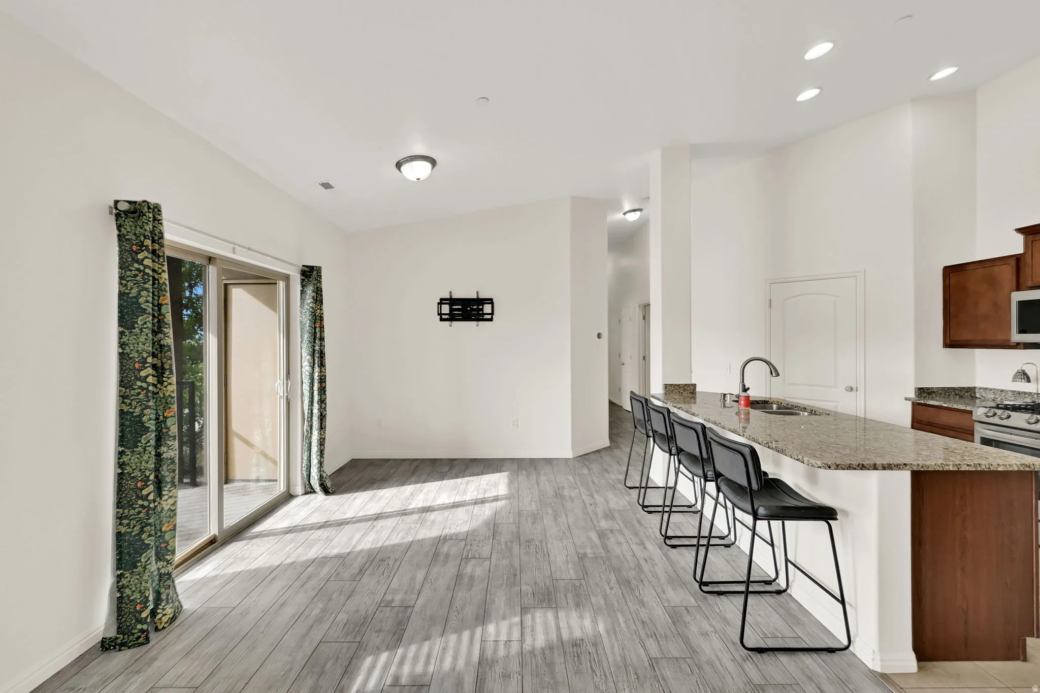 Open-concept living space with wood-finish flooring, sliding glass doors, recessed lighting, and a kitchen island featuring a sink and bar seating