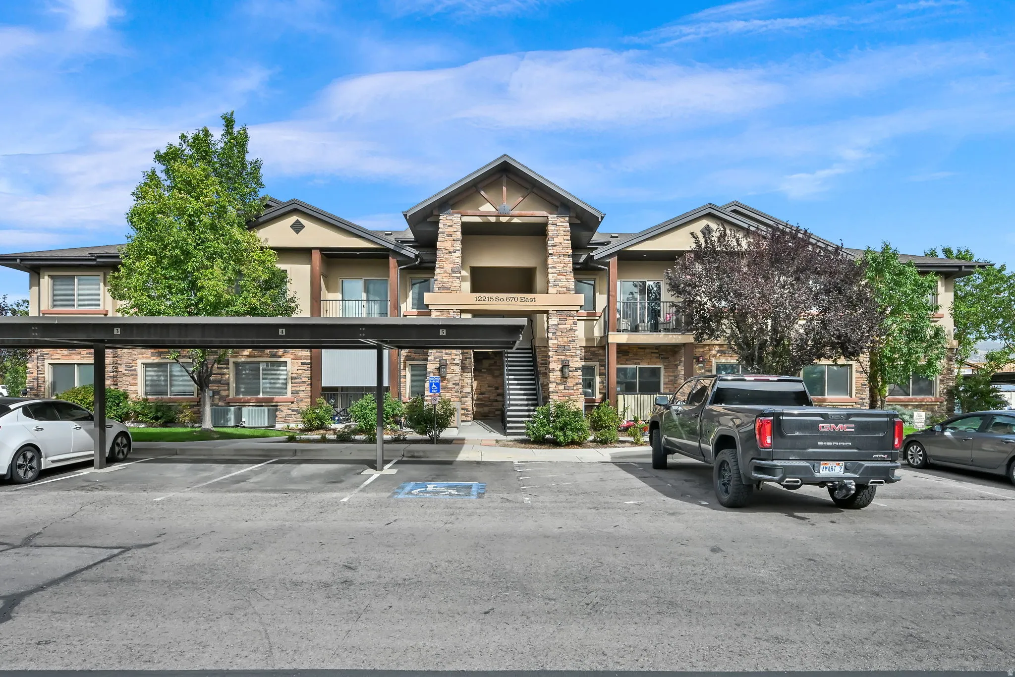 Multi-story building featuring stone and stucco exterior, covered parking, mature landscaping, and balconies