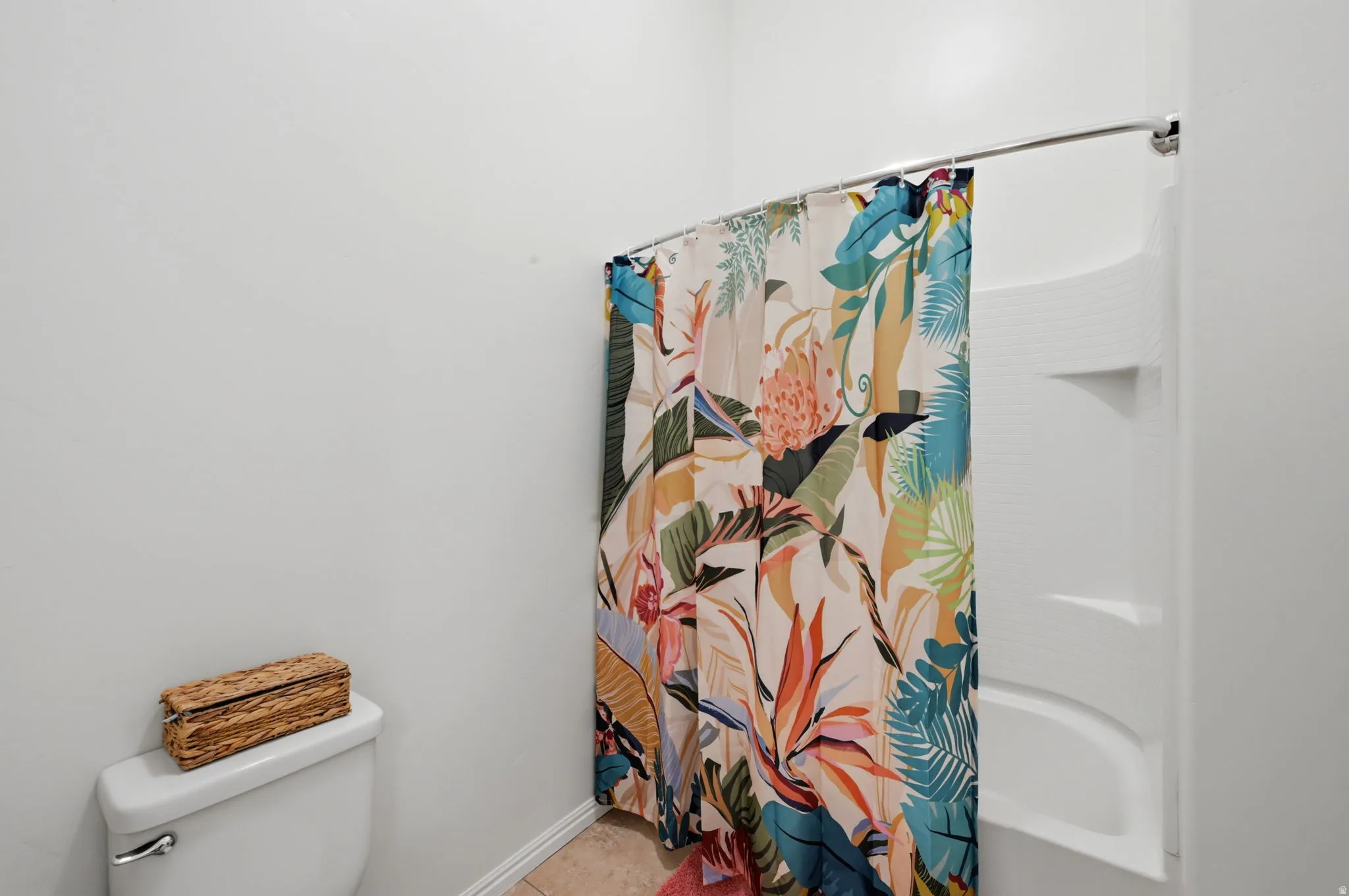Bathroom featuring a white toilet, light-toned tile flooring, and a white shower/tub combination with integrated shelving