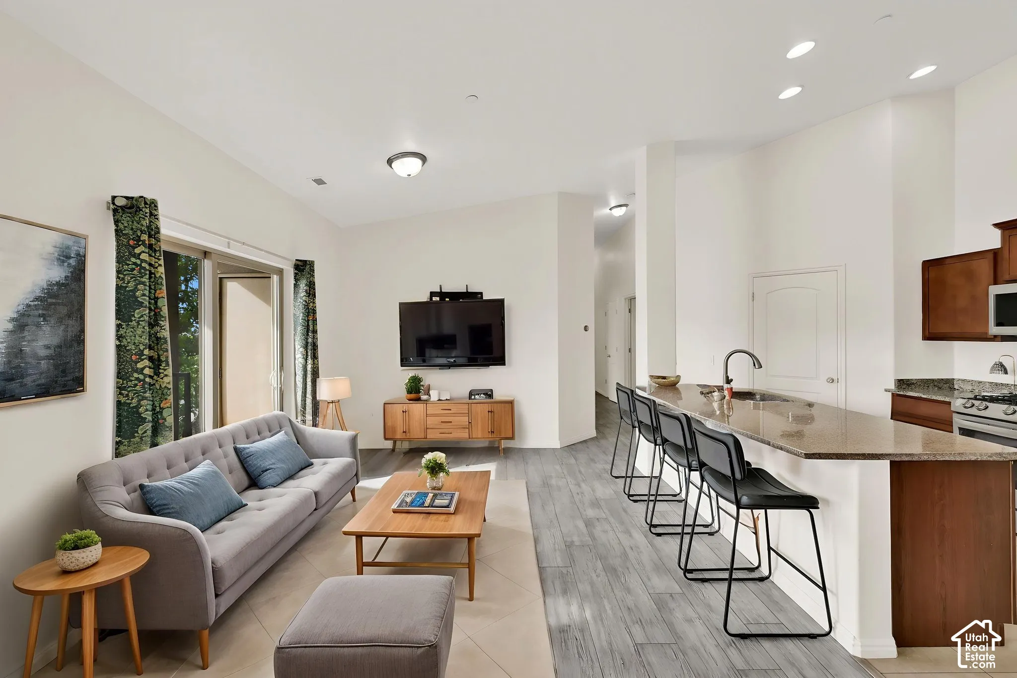 Open-concept living space featuring high ceilings, wood-finish flooring, a kitchen island with seating, and a stainless steel gas range