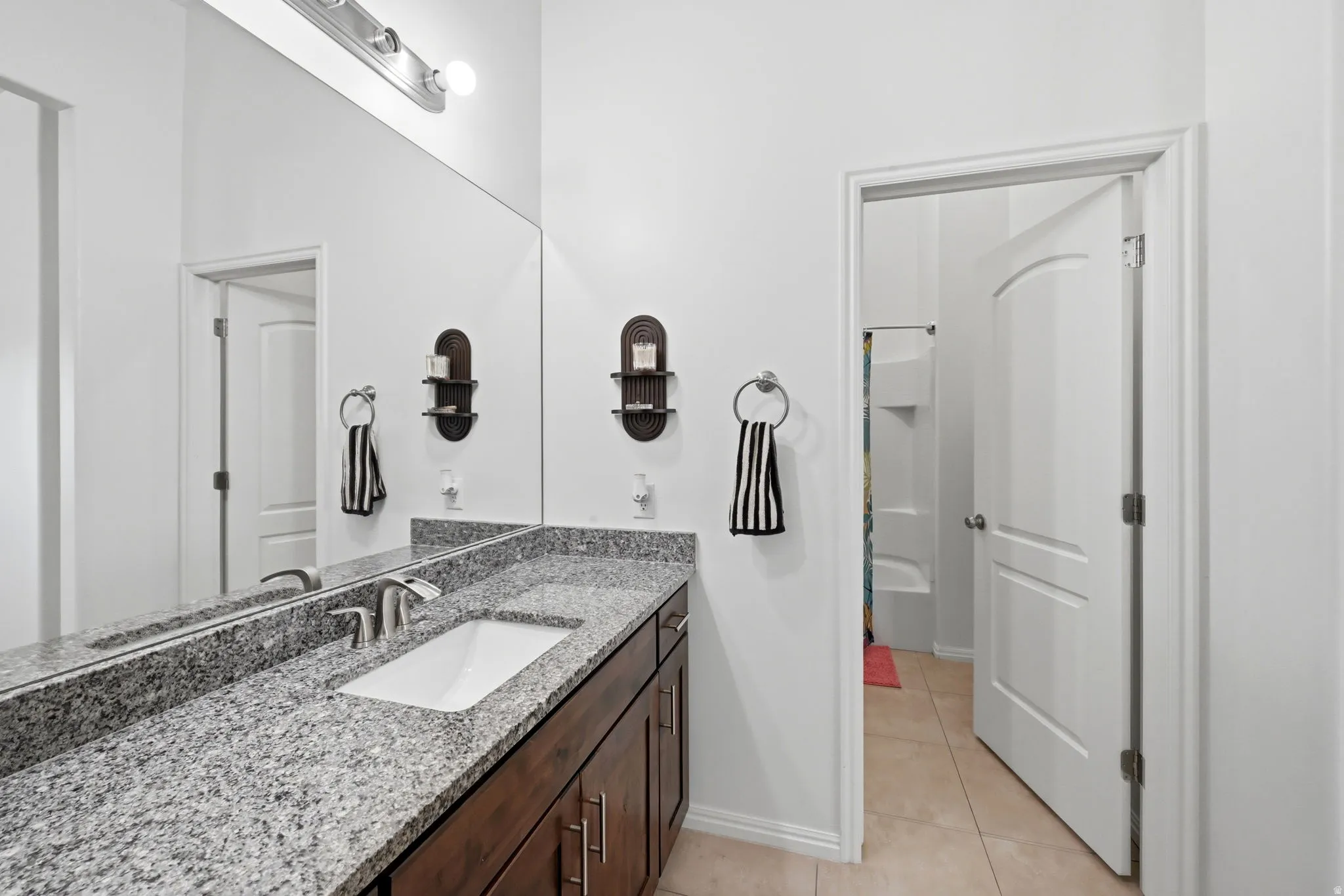 Bathroom featuring a vanity with a large mirror, granite countertop, dual sinks, dark wood cabinetry, and brushed nickel fixtures