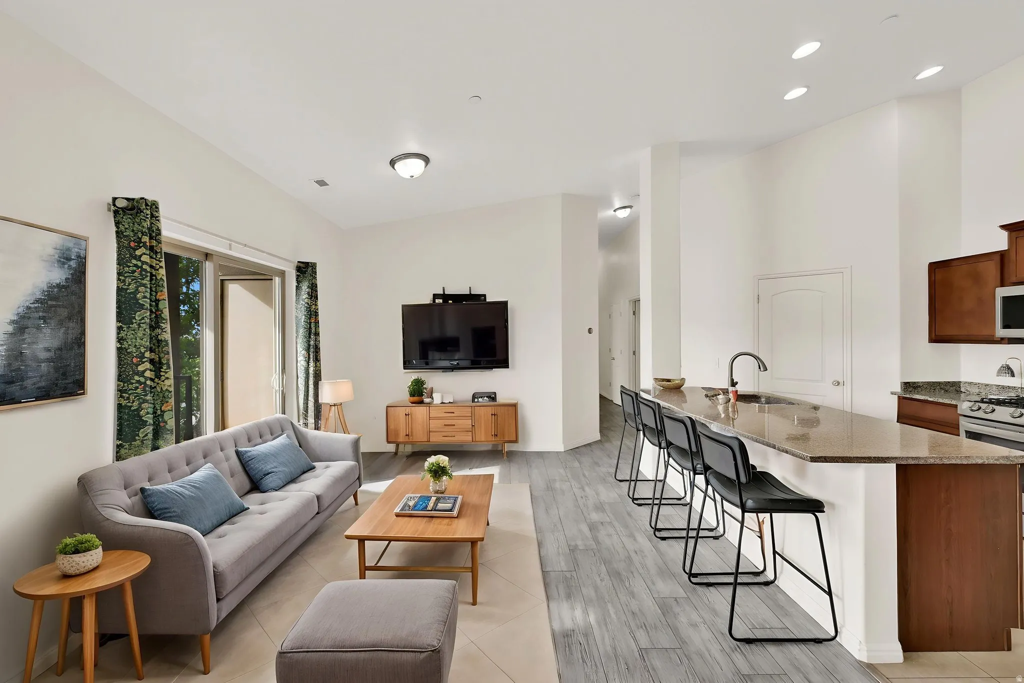 Open-concept living space featuring high ceilings, wood-finish flooring, a kitchen island with seating, and a stainless steel gas range