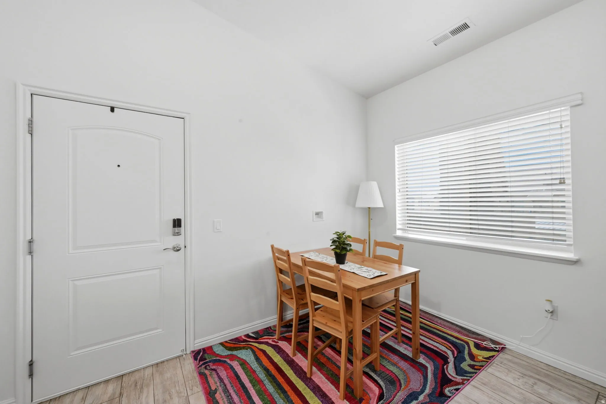Bright interior space featuring a white paneled door with smart lock, wood-finish flooring, and a window with horizontal blinds