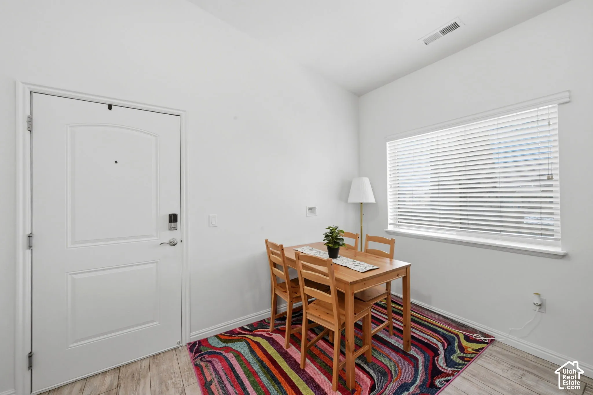 Bright interior space featuring a white paneled door with smart lock, wood-finish flooring, and a window with horizontal blinds