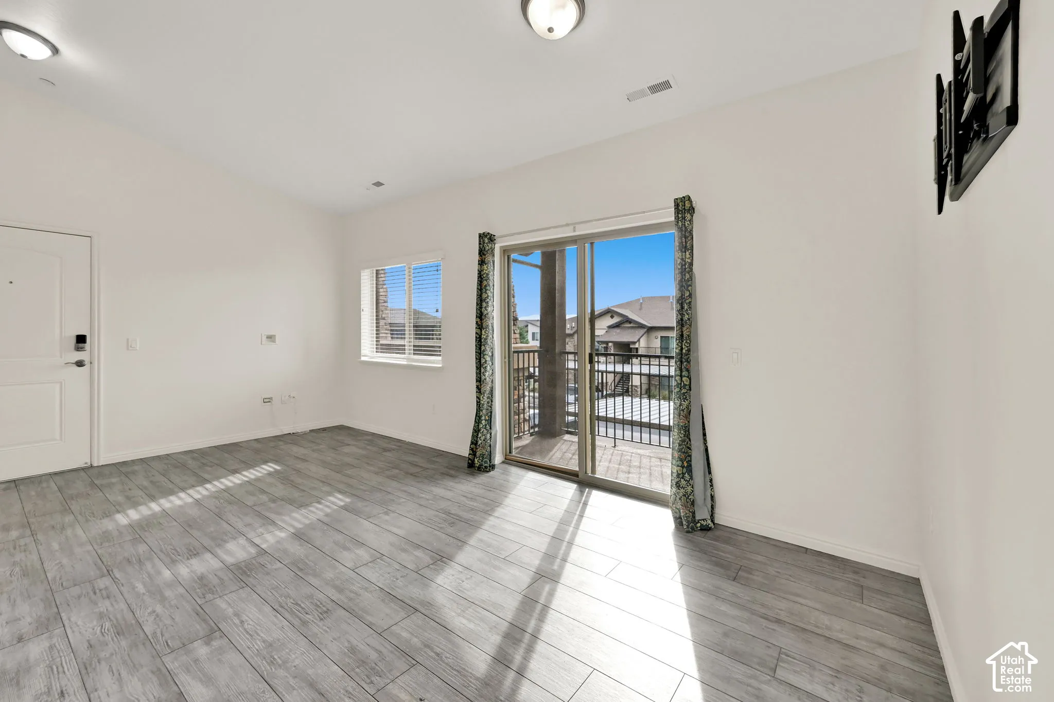 Wood-finish flooring, white walls, built-in wall mount, sliding glass door with balcony, and a window with blinds