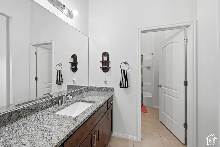 Bathroom featuring a vanity with a large mirror, granite countertop, dual sinks, dark wood cabinetry, and brushed nickel fixtures