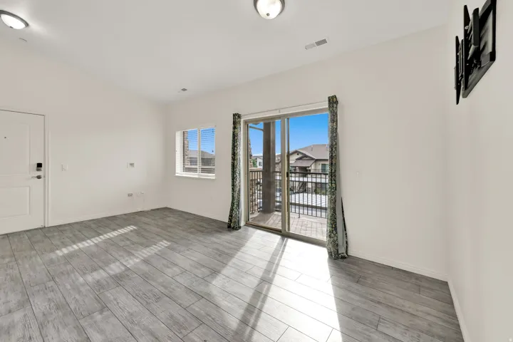 Wood-finish flooring, white walls, built-in wall mount, sliding glass door with balcony, and a window with blinds